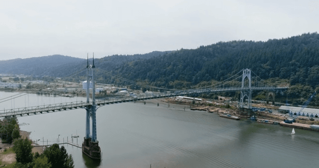 A large bridge spanning a river with forested hills