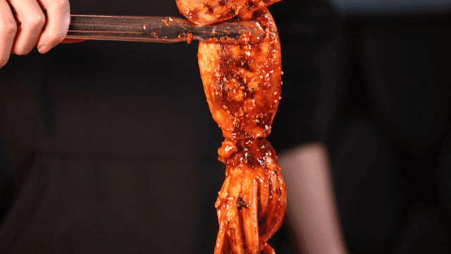 Spicy stir-fried squid seafood stew lifted with tongs