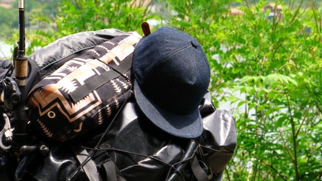 Backpack with hat and fishing rod by lush greenery