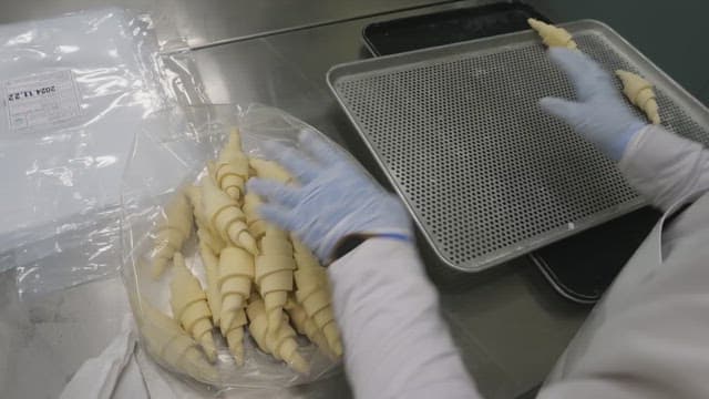 Placing croissant dough on a baking tray in an industrial kitchen