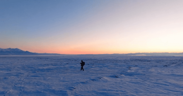Person walking on a snowy field at sunrise