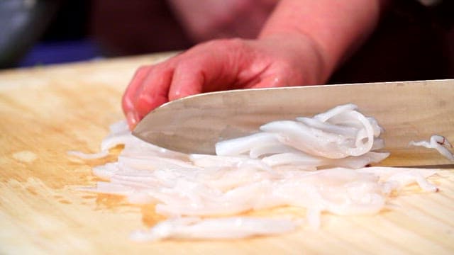 Slicing fresh swordtip squid on a wooden cutting board