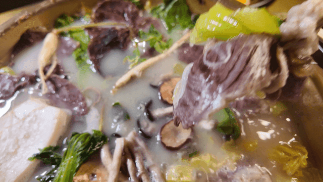 Chopsticks picking up Hanwoo beef and bok choy from hot pot