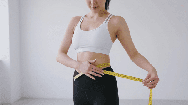 Thin woman measuring her waist with tape measure