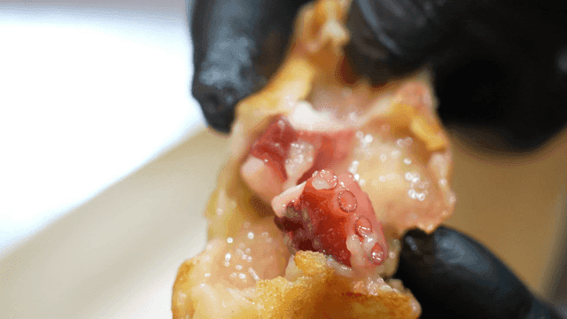 Gloves holding torn piece of takoyaki