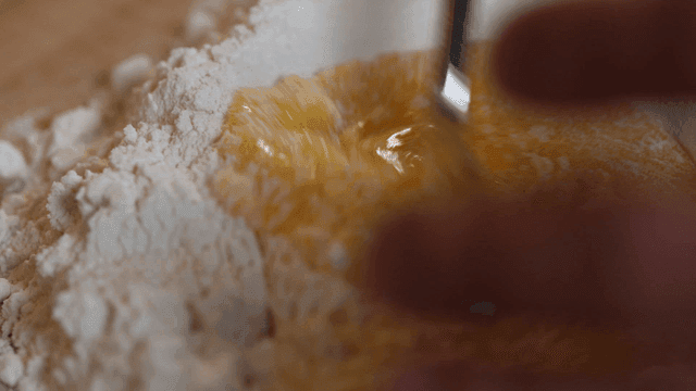 Fork mixing flour and eggs on wooden cutting board