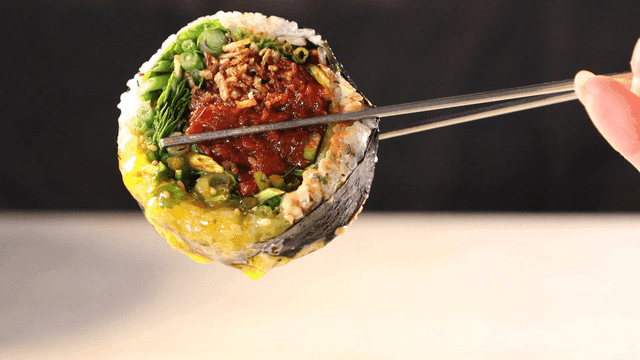 Chopsticks lifting raw beef gimbap filled with colorful ingredients