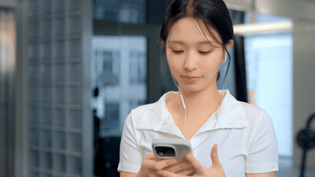 Young woman using smartphone with earphones at gym