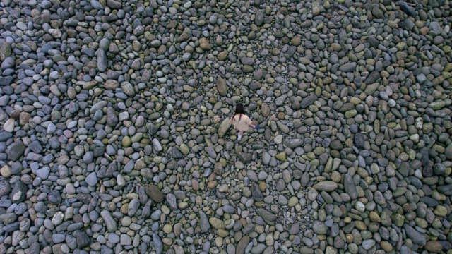 Person Walking on Pebble Beach with Shoes in Hand