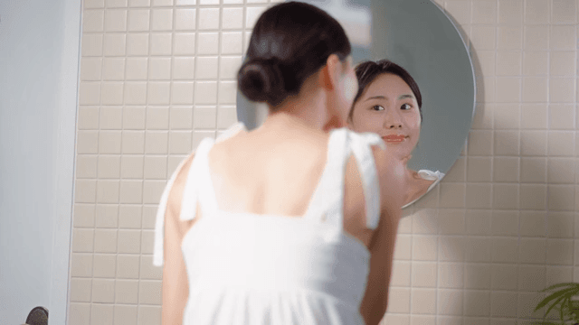 Woman examining her skin in a bathroom mirror