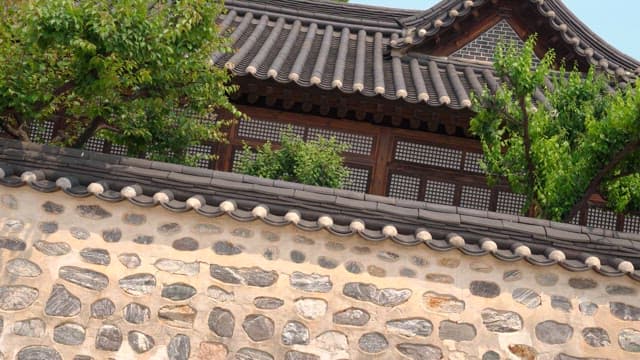 맑은 날 돌담과 푸른 나무가 어우러진 한국 전통 한옥