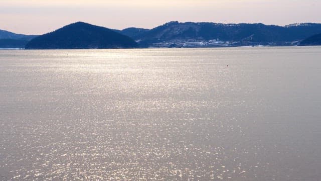 Sparkling sea with distant hills under cloudy sky