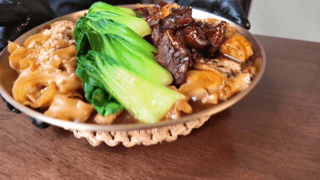 Server serving dish topped with bok choy and marinated short ribs at restaurant
