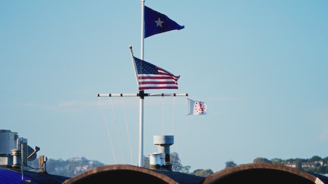 Flags waving over industrial barrels against sky