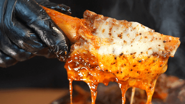 Hand holding up spicy braised short ribs covered in cheese