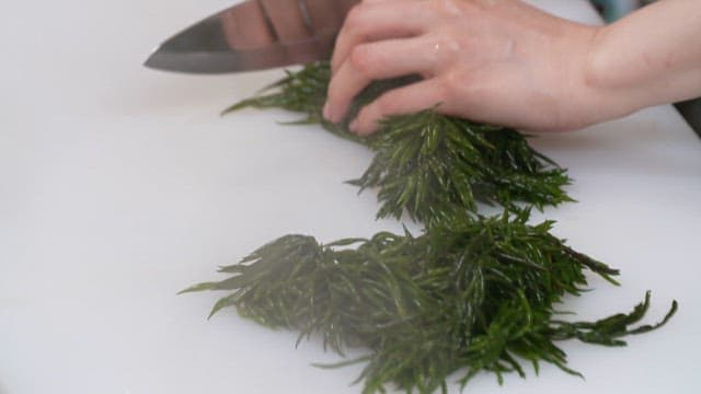 실내 주방에서 흰 도마 위에 신선한 해초를 써는 모습