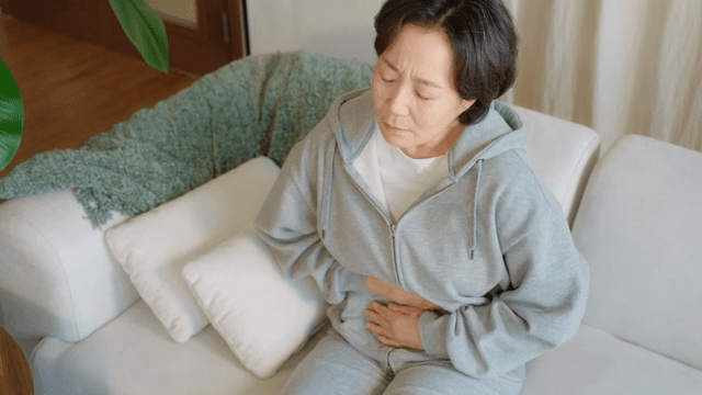 소파에 앉아 배를 잡고 있는 여성