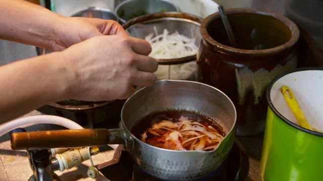 작은 냄비에서 끓고 있는 양파 위에 베이컨을 추가하는 모습