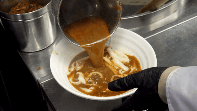 Pouring spicy broth over noodles