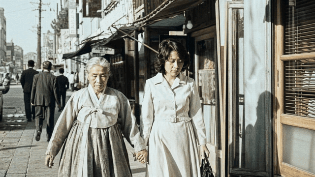 Woman holding hands and elderly person wearing Hanbok walking on city street in 1970s