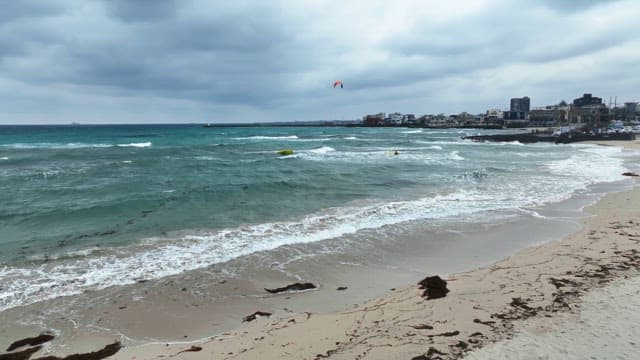 Waves crashing on a beach with kite surfers