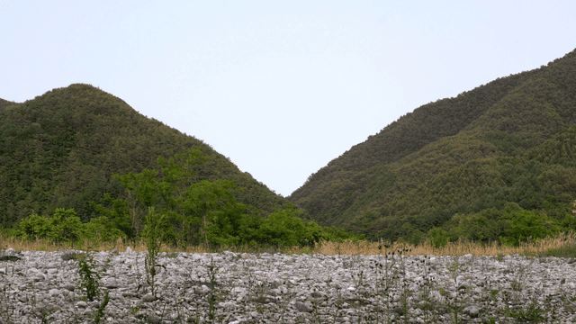 Green hills and mountains behind a gravel field