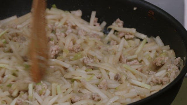 검은색 프라이팬에서 무와 고기를 볶는 모습