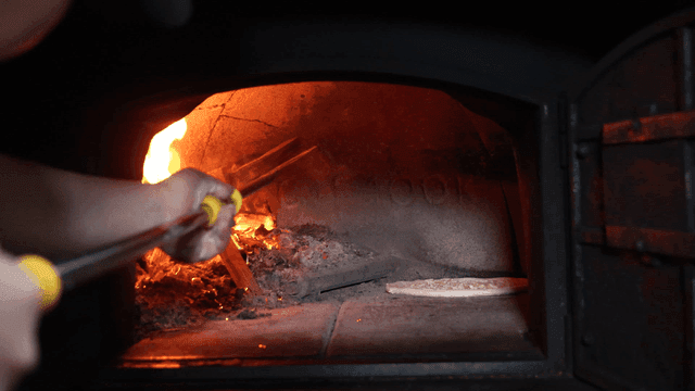 Pizza in wood-fired oven with firewood