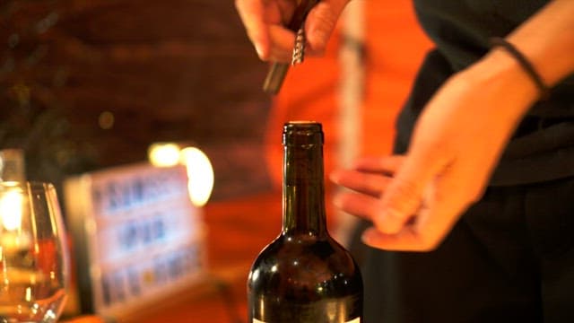 Person opening a wine bottle with a corkscrew