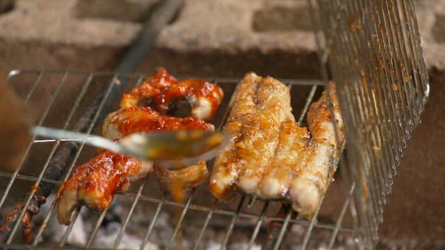 Applying sauce to eel grilled over charcoal