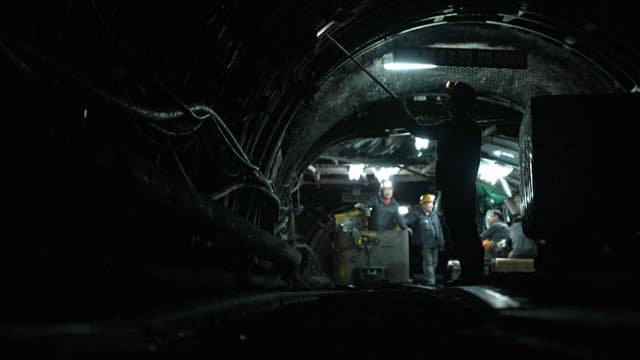 Miners working in a dark underground tunnel of coal mine