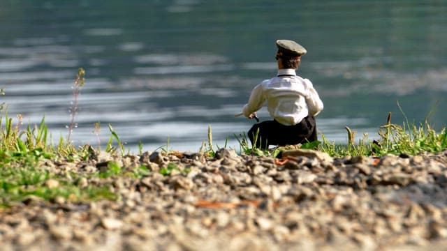 Figure resembling the back of a man fishing on a calm lake in the afternoon