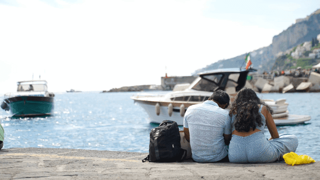 Back view of couple sitting in sea with boat passing by