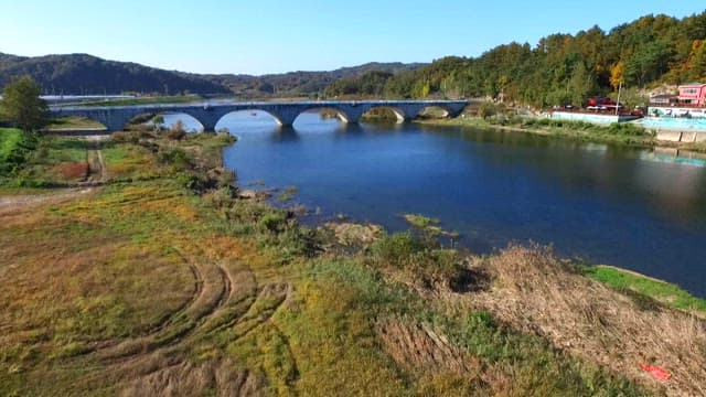 People performing traditional performances on the riverside with a historic bridge