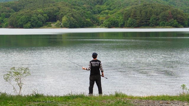 Person fishing by the serene lake on a cloudy day