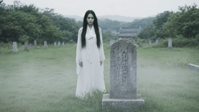 Woman in white mourning clothes standing in graveyard