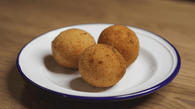 흰 접시에 놓인 세 개의 아란치니 튀김볼