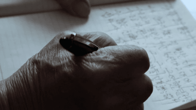 An elderly hand writing in a notebook