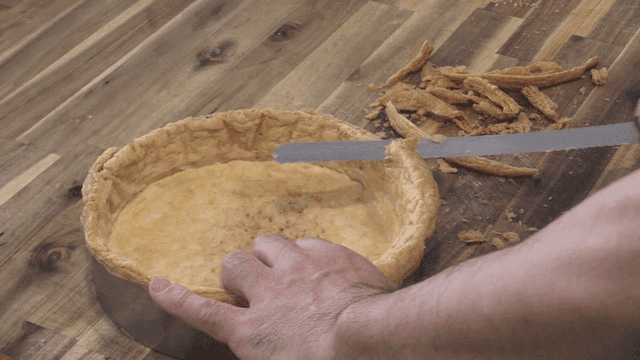 Bread knife trimming pie crust on wooden table