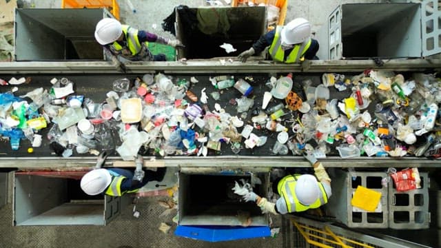 Plastic waste sorting process in a recycling plant with workers wearing safety gear