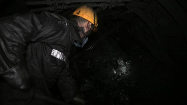 Miner digging inside a dark coal mine tunnel, illuminated by dim lighting