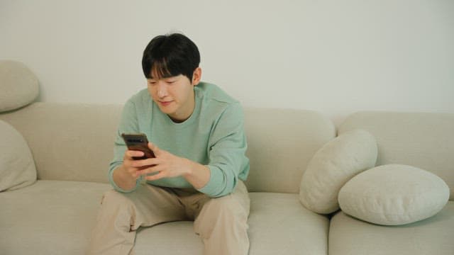 소파에 앉아 스마트폰을 사용하는 남자