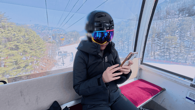 Woman wearing helmet looking at her cell phone while riding up ski resort cable car.