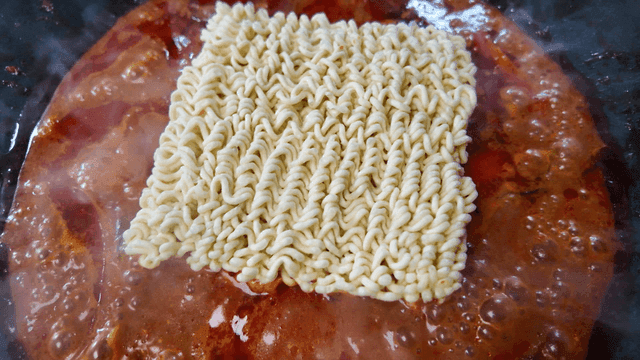 Ramen noodles boiling in spicy chicken stew broth