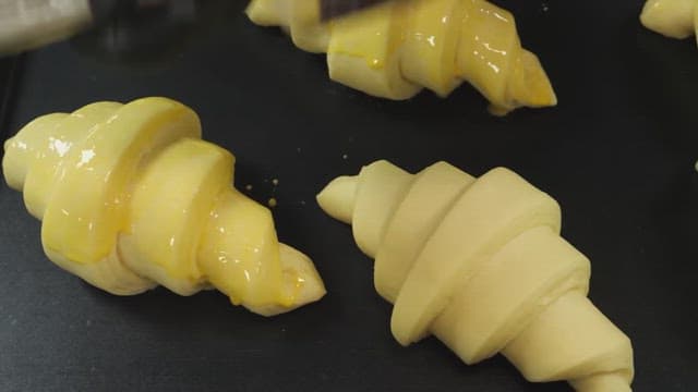 Brushing egg wash on croissant dough on a baking tray