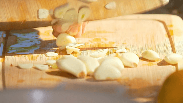 Garlic being sliced on a wooden board