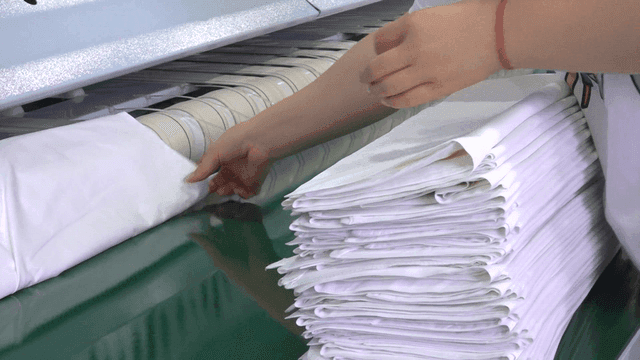 Worker stacking neatly folded sheets in laundry factory
