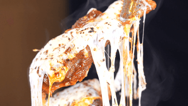 Tongs lifting spicy braised short ribs covered in cheese