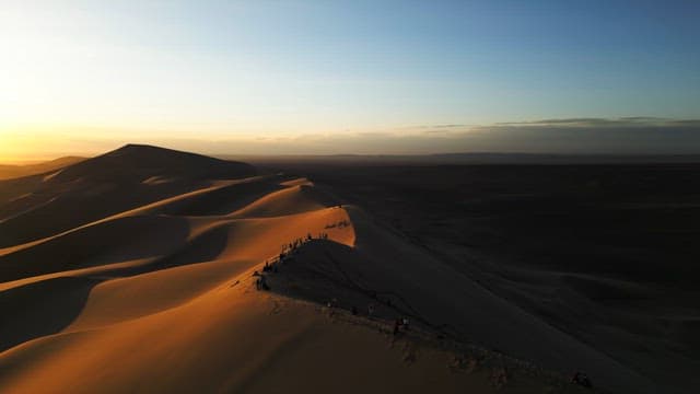 People walking on sand dunes at sunset