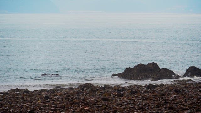 Calm rocky beach facing a serene ocean under a cloudy sky